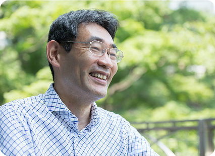 眼鏡をかけた男性が自然の中で柔らかく微笑み、穏やかな雰囲気が伝わる屋外ポートレート