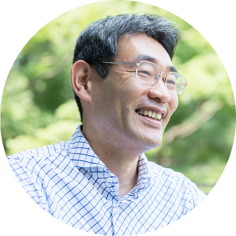 眼鏡をかけた男性が自然の中で柔らかく微笑み、穏やかな雰囲気が伝わる屋外ポートレート